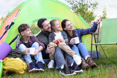 Photo of Happy family spending time together with camping tent, tourist equipment and mugs of hot drink outdoors
