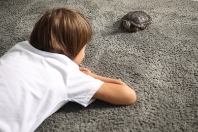 Photo of Little boy and cute turtle on grey carpet, closeup. Domestic pet