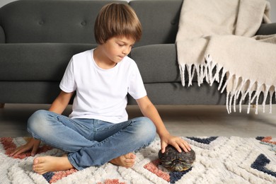 Photo of Little boy stroking his turtle on floor at home. Domestic pet