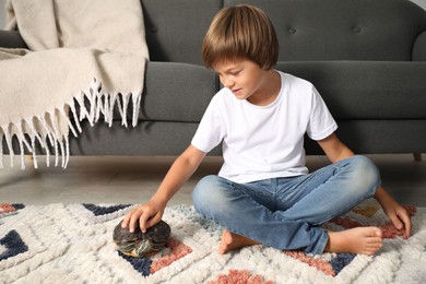 Photo of Little boy stroking his turtle on floor at home. Domestic pet