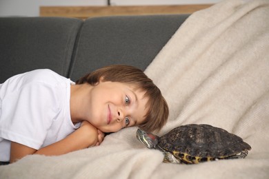 Photo of Little boy and cute turtle on sofa at home. Domestic pet