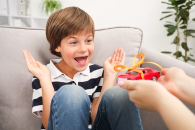 Photo of Dreams come true. Mother presenting toy car to her happy son at home, closeup