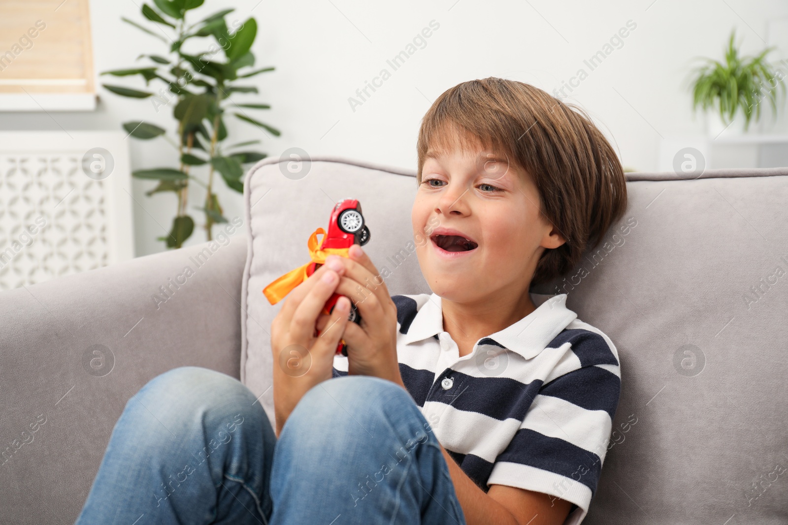 Photo of Dreams come true. Happy boy with toy car on armchair at home