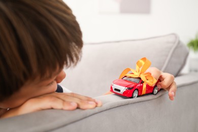 Photo of Dreams come true. Little boy playing with toy car on armchair at home, closeup