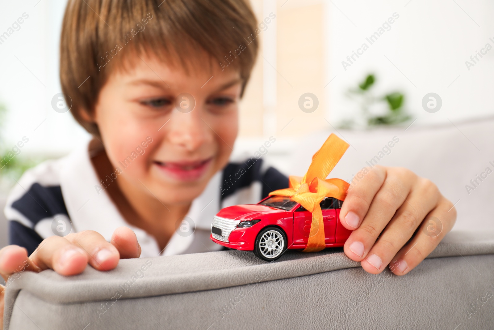 Photo of Dreams come true. Happy boy playing with toy car on armchair at home, closeup