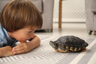 Photo of Little boy and cute turtle on floor at home, closeup. Domestic pet