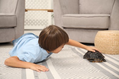 Photo of Little boy stroking his turtle on floor at home. Domestic pet