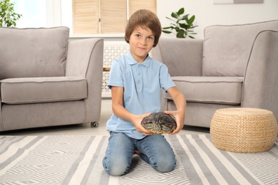Photo of Little boy holding his turtle pet on floor at home