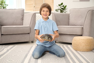 Photo of Happy boy holding his turtle pet on floor at home