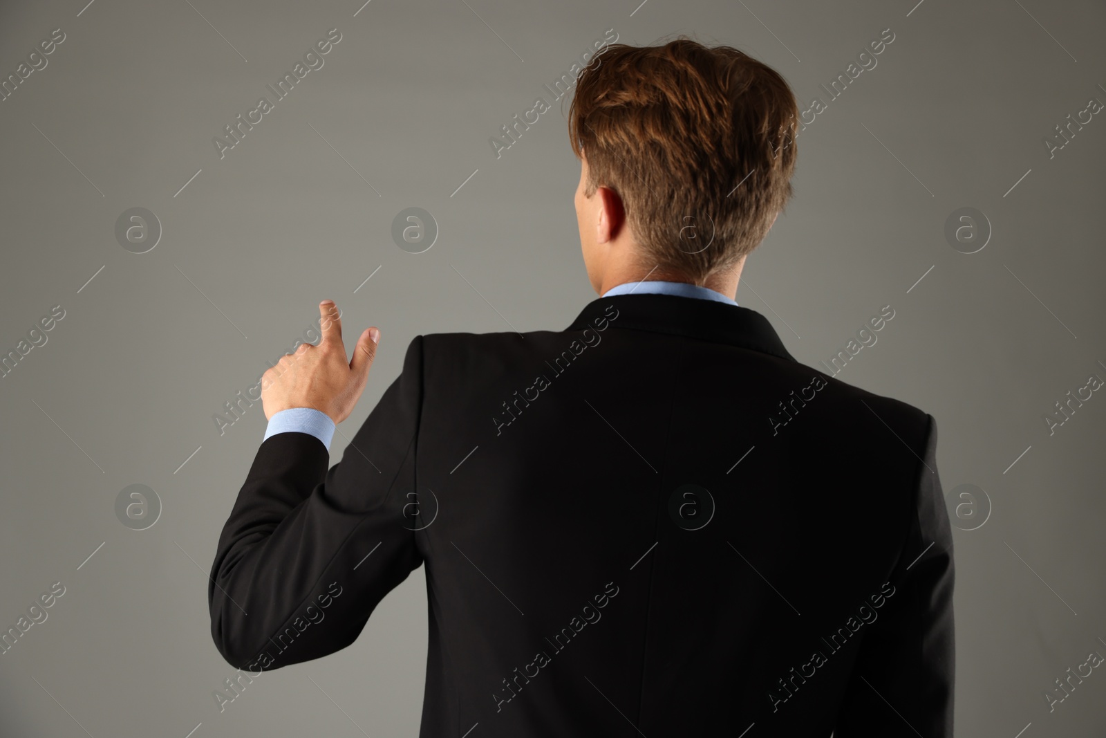 Man touching something on grey background, back view Photo of Man touching something on grey background, back view