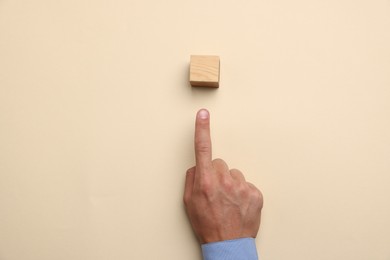 Photo of Man touching wooden cube on beige background, top view