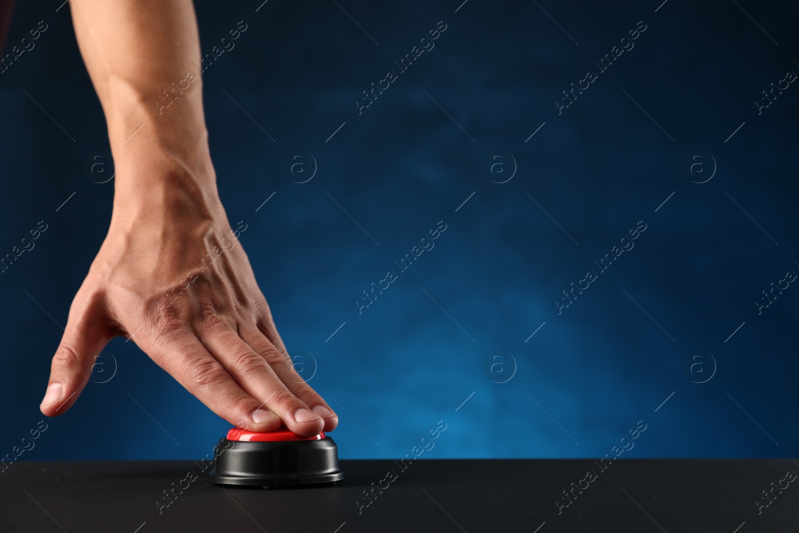 Man pressing button on black table against blue background, closeup. Space for text Photo of Man pressing button on black table against blue background, closeup. Space for text