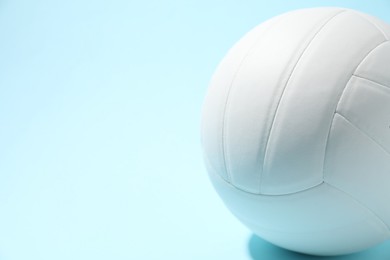 Photo of White volleyball ball on light blue background, closeup. Space for text