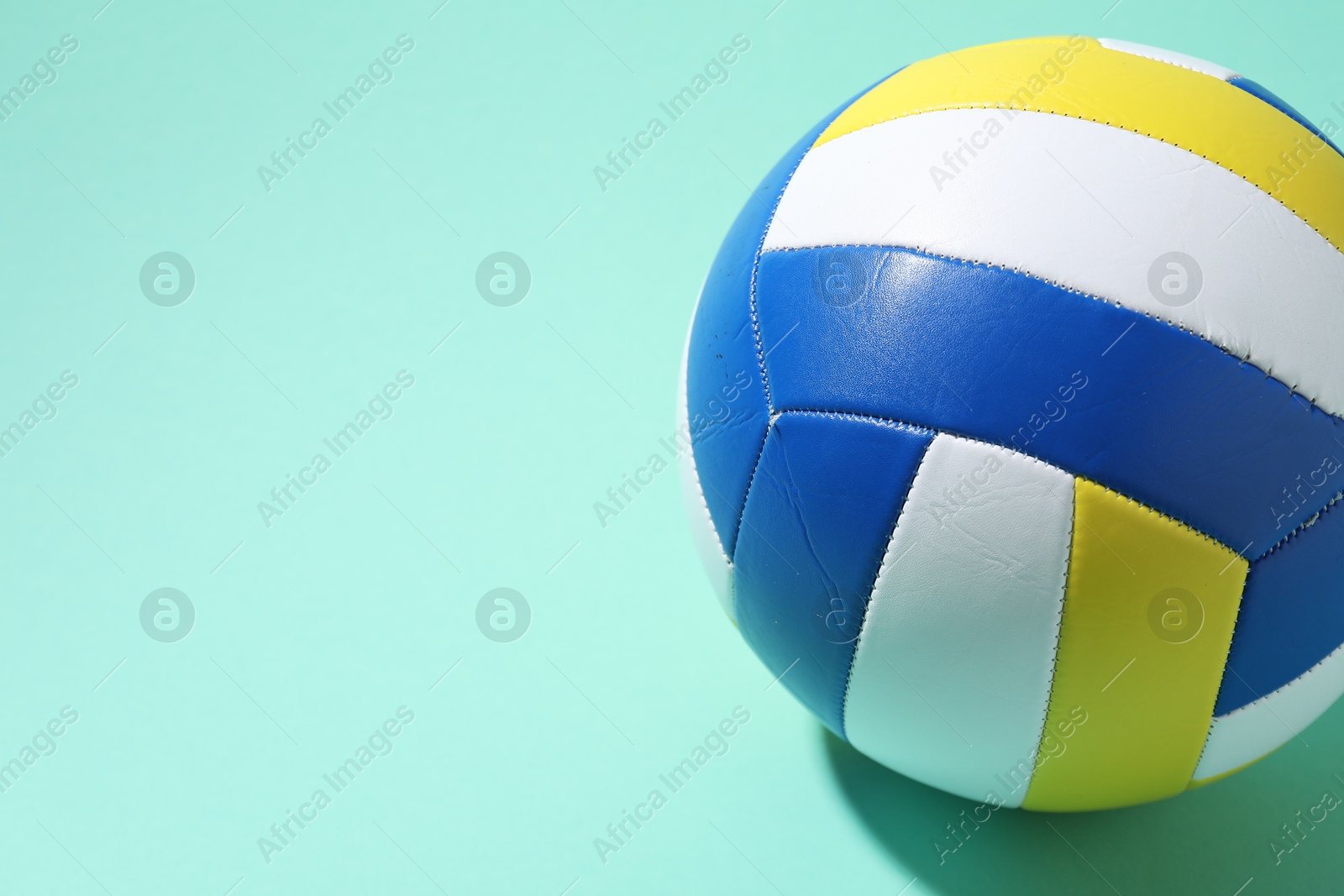 Photo of Colorful volleyball ball on turquoise background. Space for text