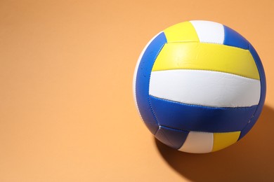Photo of Colorful volleyball ball on pale orange background, above view. Space for text