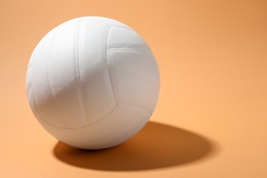 Photo of White volleyball ball on pale orange background. Space for text