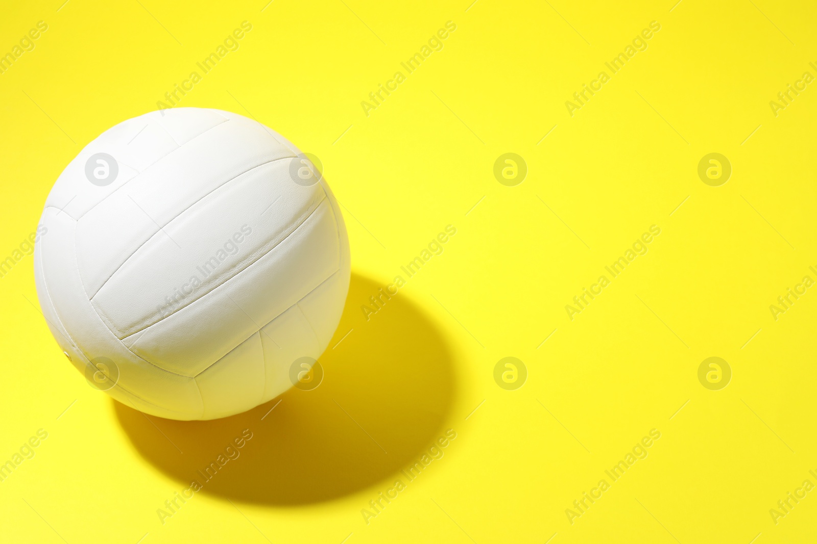 Photo of White volleyball ball on yellow background, above view. Space for text