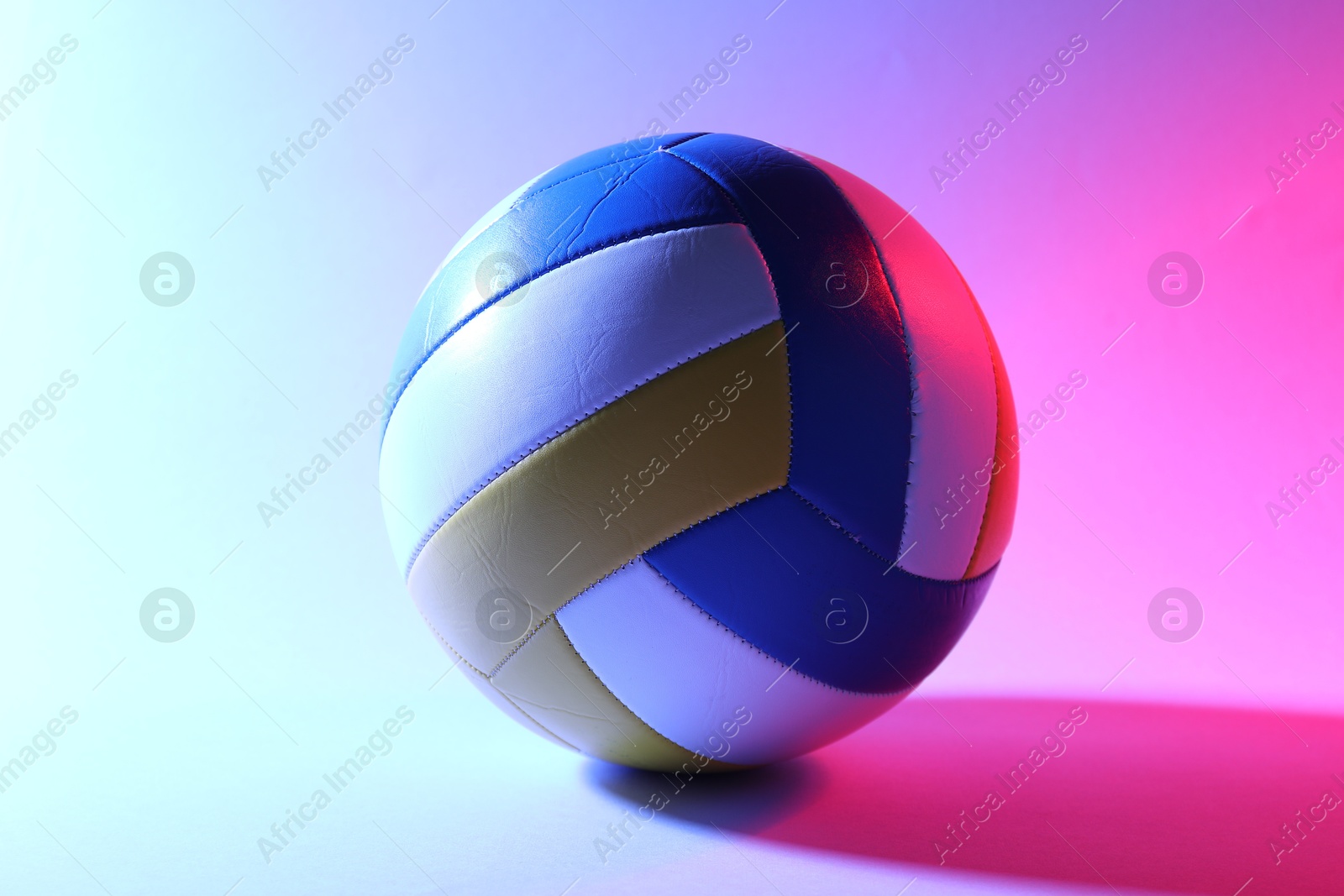 Photo of Colorful volleyball ball on light background in color lights
