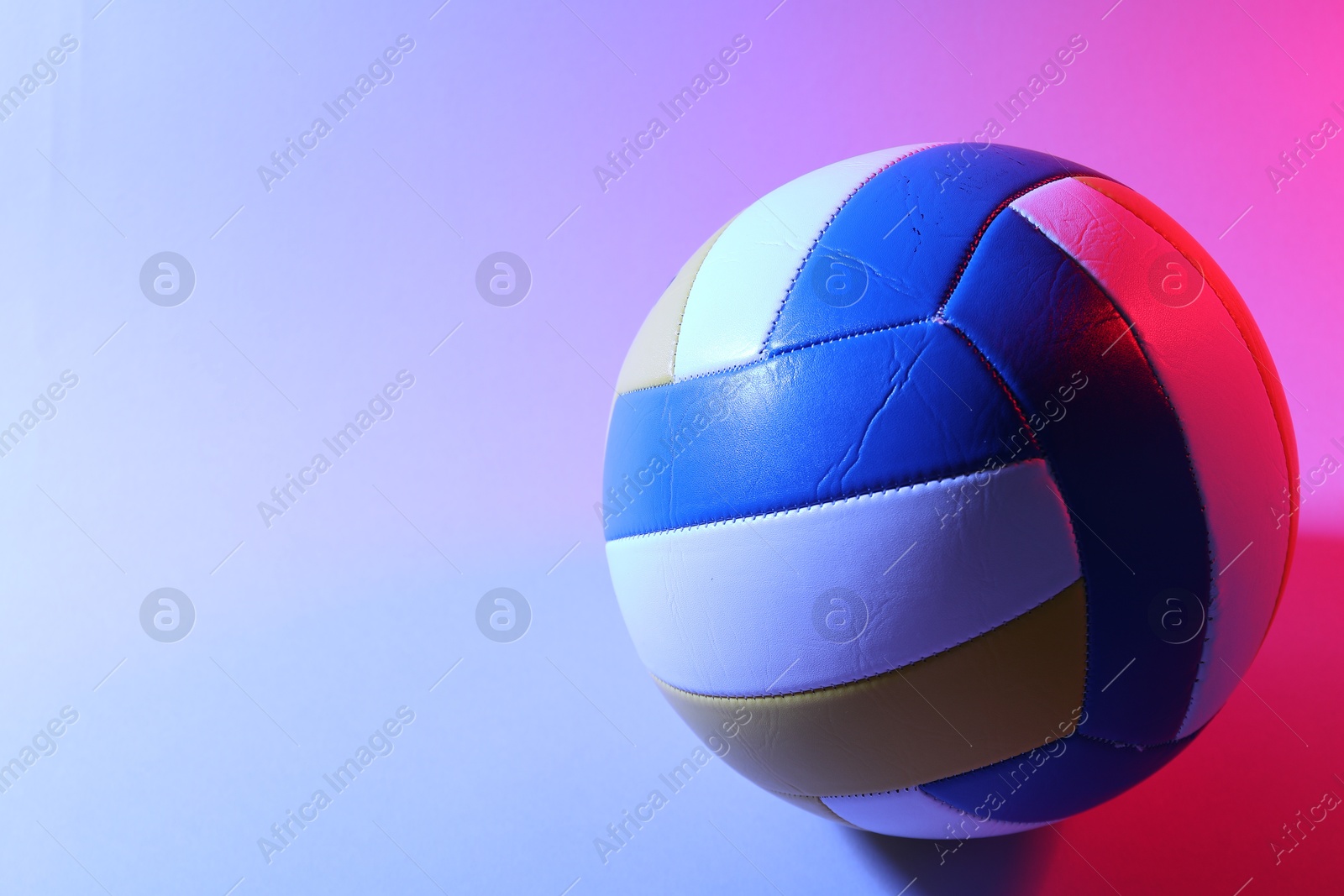 Photo of Colorful volleyball ball on light background in color lights. Space for text