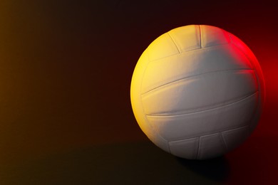 Photo of White volleyball ball on dark background in color lights. Space for text