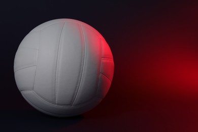 Photo of White volleyball ball on dark background in color light. Space for text