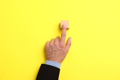 Photo of Man touching wooden cube on yellow background, top view