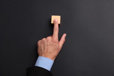 Photo of Man touching wooden cube on black background, top view