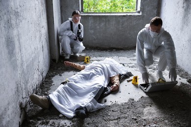 Photo of Forensic experts working at crime scene with dead man's body inside abandoned building