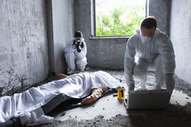 Photo of Forensic experts working at crime scene with dead man's body inside abandoned building