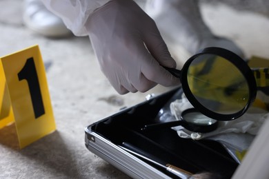 Photo of Forensic expert with magnifying glass working at crime scene indoors, closeup