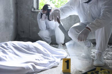 Photo of Forensic experts working at crime scene with dead body inside abandoned building