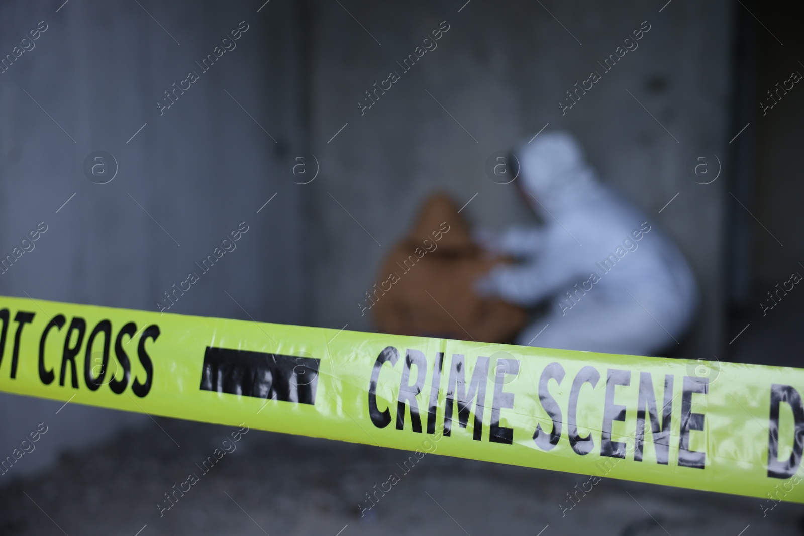 Photo of Forensic expert working at crime scene with dead body inside abandoned building, focus on yellow police tape