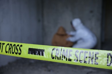 Photo of Forensic expert working at crime scene with dead body inside abandoned building, focus on yellow police tape