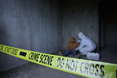 Photo of Forensic expert working at crime scene with dead body inside abandoned building, focus on yellow police tape