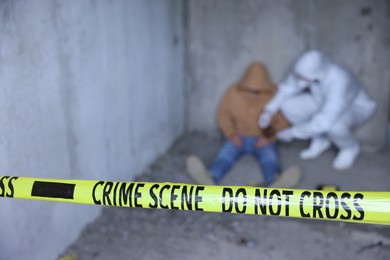 Photo of Forensic expert working at crime scene with dead body inside abandoned building, focus on yellow police tape