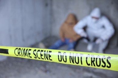 Photo of Forensic expert working at crime scene with dead body inside abandoned building, focus on yellow police tape