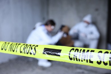 Photo of Forensic experts working at crime scene with dead body inside abandoned building, focus on yellow police tape