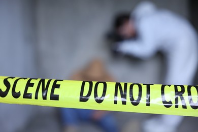 Photo of Forensic expert working at crime scene with dead body inside abandoned building, focus on yellow police tape