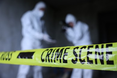 Photo of Forensic experts working at crime scene inside abandoned building, focus on yellow police tape