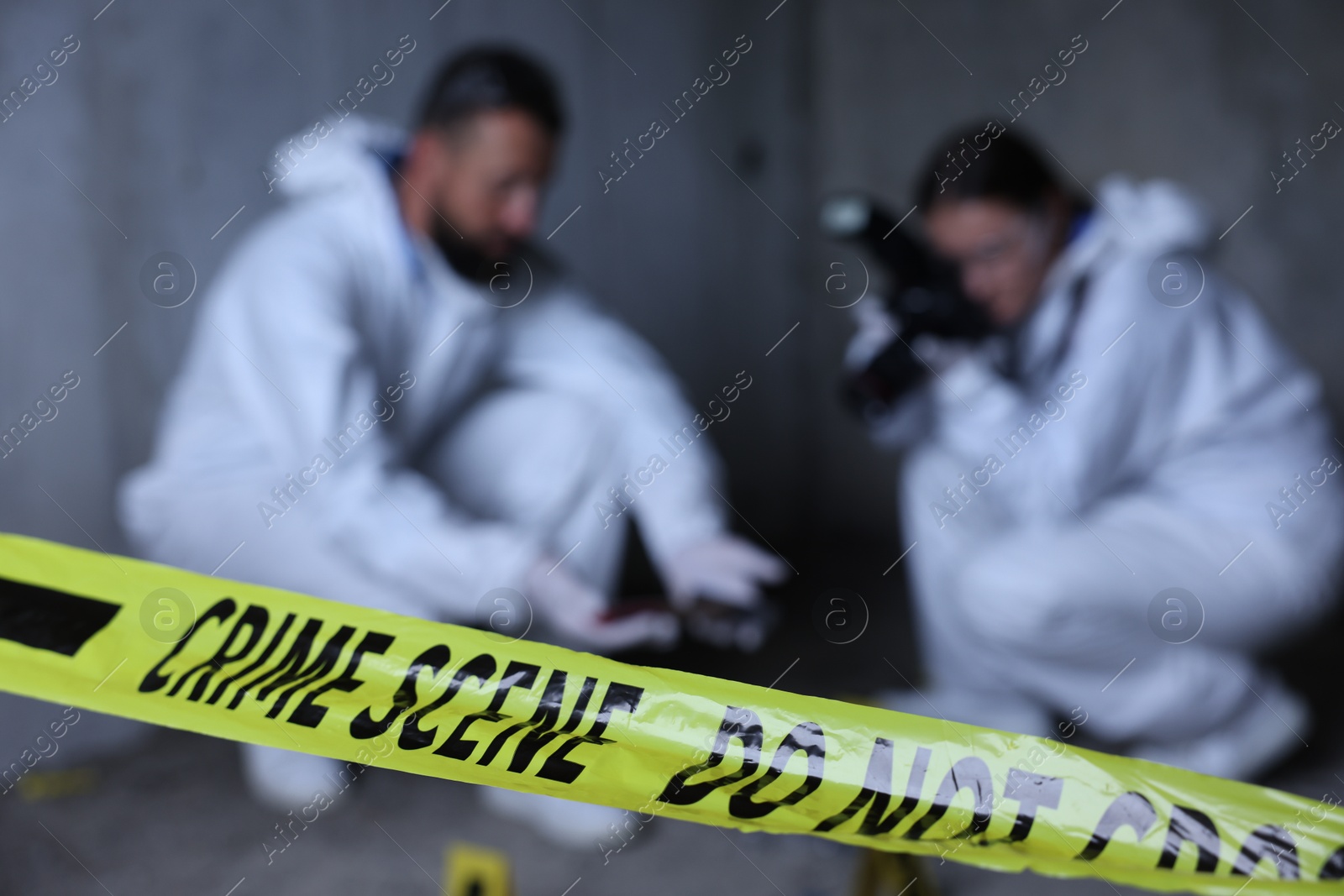Forensic experts working at crime scene inside abandoned building, focus on yellow police tape Photo of Forensic experts working at crime scene inside abandoned building, focus on yellow police tape