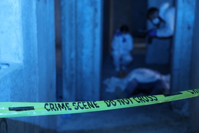 Photo of Forensic experts working at crime scene with dead body inside abandoned building, focus on yellow police tape