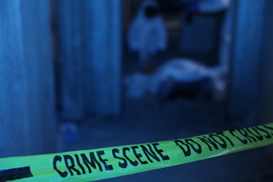 Photo of Forensic experts working at crime scene with dead body inside abandoned building, focus on yellow police tape