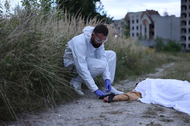 Photo of Forensic expert working at crime scene with dead body outdoors