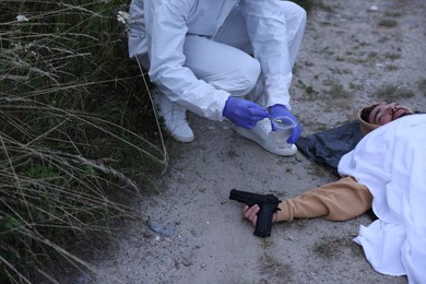 Photo of Forensic expert working at crime scene with dead body outdoors, closeup