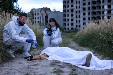 Photo of Forensic experts working at crime scene with dead body outdoors