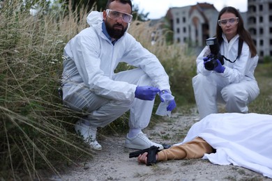 Photo of Forensic experts working at crime scene with dead body outdoors