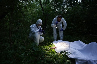 Photo of Forensic experts working at crime scene with dead body outdoors