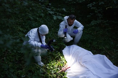 Photo of Forensic experts working at crime scene with dead body outdoors