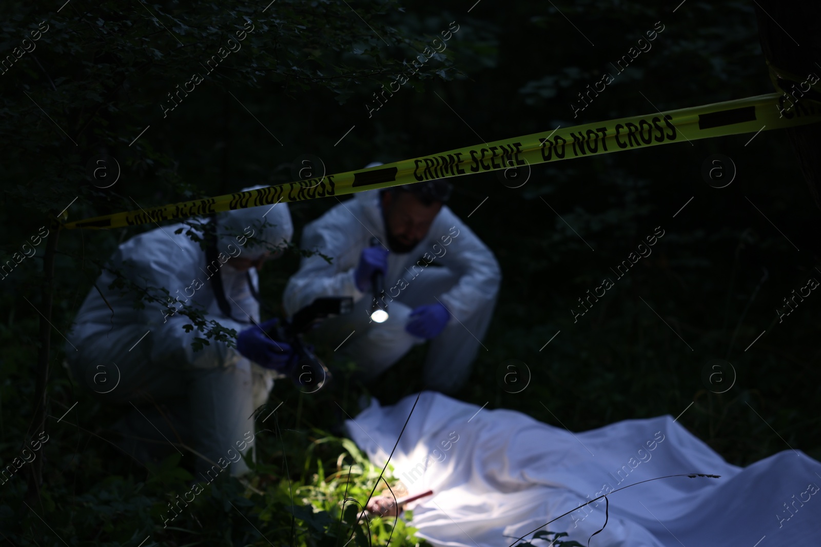 Forensic experts working at crime scene with dead body outdoors, focus on yellow police tape Photo of Forensic experts working at crime scene with dead body outdoors, focus on yellow police tape