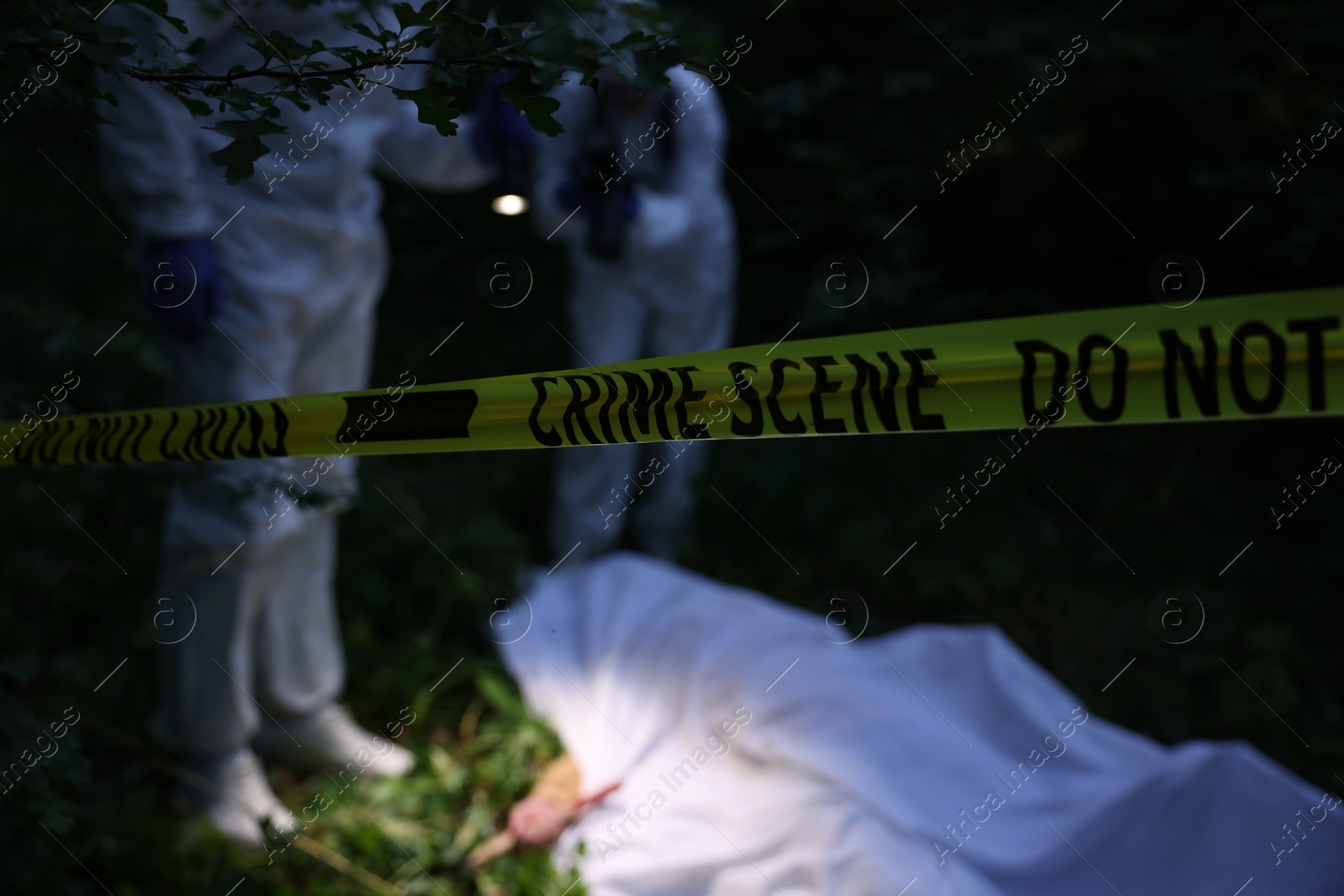 Forensic experts working at crime scene with dead body outdoors, focus on yellow police tape Photo of Forensic experts working at crime scene with dead body outdoors, focus on yellow police tape